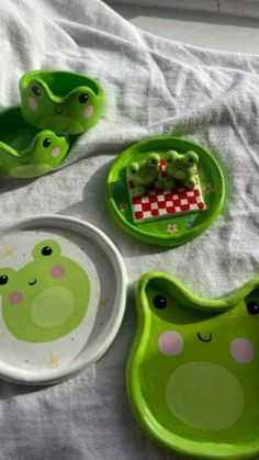 three plates and two bowls on a bed with white sheets, one has green frog design