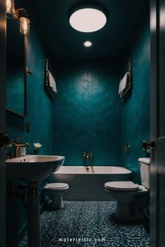 A small, modern bathroom with dark teal walls, a white bathtub, sink, and toilet, and brass fixtures. Bathroom Makeover Ideas