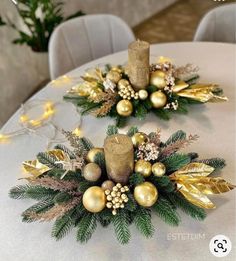 two christmas decorations are sitting on top of a white tablecloth with gold balls and greenery