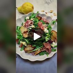 a white plate topped with lots of salad next to a yellow pear on top of a table