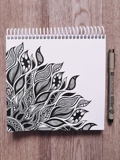 a spiral notebook with black and white designs on the cover next to a marker pen