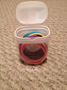 a plastic container filled with lots of different colored rubber bands on top of a carpet