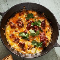 a skillet filled with food on top of a wooden table next to toasted bread