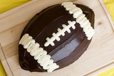 a chocolate football cake with icing on a cutting board next to a yellow tablecloth