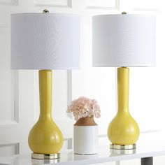 two yellow vases with flowers in them sitting on a table next to a lamp