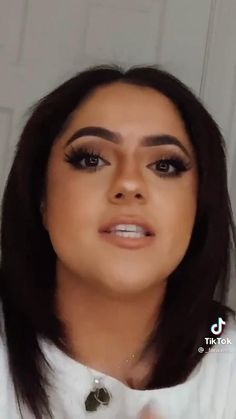 a woman with long dark hair wearing a white shirt and black eye makeup looks at the camera