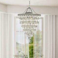 a chandelier hanging from the ceiling in a living room with white walls and curtains