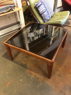 a glass coffee table sitting on top of a floor next to a green chair and pillow