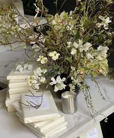 a vase with white flowers on top of a table next to some books and papers