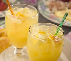 two glasses filled with orange juice sitting on top of a table next to plates of fruit