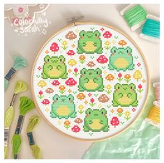 a cross stitch pattern with frog designs on it and some thread spools next to it