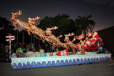 a parade float with santa claus and reindeers on it's side at night