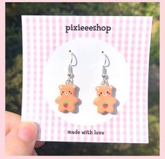 a pair of earrings featuring a teddy bear with strawberry in its mouth on a pink and white checkered background