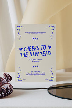 there is a card that says cheers to the new year next to some glassware