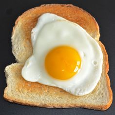 an egg in the middle of a piece of bread on a black surface with a fork