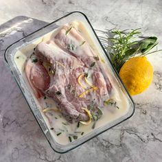 raw chicken with lemons and herbs in a glass dish on a marble counter top