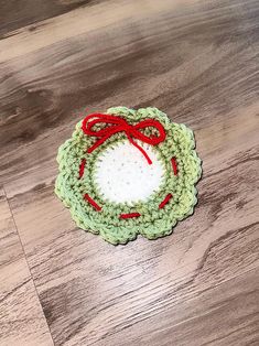 a green crocheted doily with a red bow on it sitting on a wooden surface