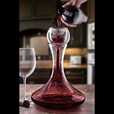 someone pouring red wine into a glass on a kitchen counter with an empty wine glass next to it