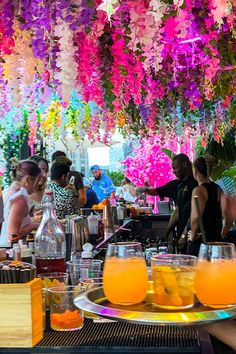 people sitting at tables with drinks and flowers hanging from the ceiling