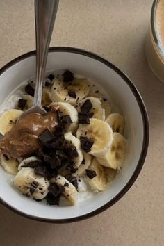 a bowl filled with ice cream and chocolate chips next to a cup of coffee on a table