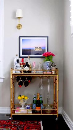 a bar cart with bottles and glasses on it in the corner of a living room