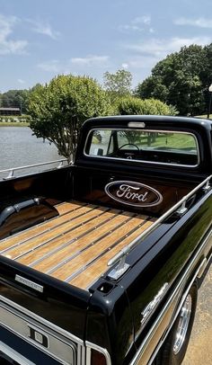 an old ford pickup truck parked next to a body of water with trees in the background