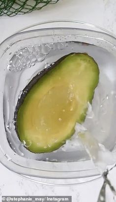 an avocado in a glass bowl with water on the side and one slice missing