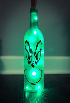 a green bottle with a face drawn on it sitting on top of a wooden table