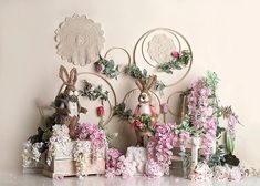 some bunny figurines are sitting on top of flowers and other decorations in front of a wall