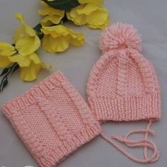 a pink knitted hat and mittens next to yellow flowers