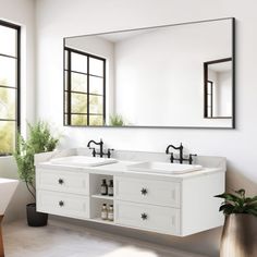 a white bathroom with two sinks and mirrors on the wall next to a potted plant