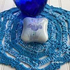 a blue vase sitting on top of a crocheted doily