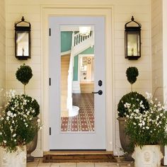 two planters with white flowers are in front of a door and some lights on the outside wall