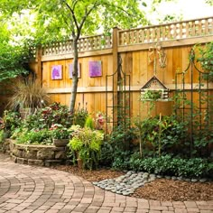 an outdoor garden with lots of plants and flowers on the side of the fenced in area