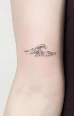 a small wave tattoo on the back of a woman's left arm, it is black and white