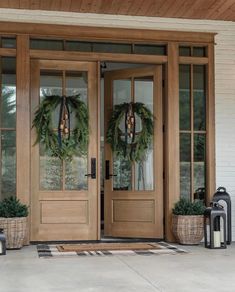 two wreaths are on the front door of a house with lanterns and lantern holders