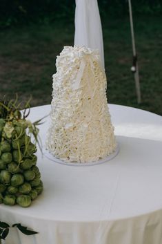 a white wedding cake sitting on top of a table next to a bunch of grapes