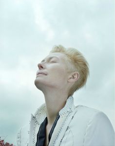 a woman with blonde hair wearing a white shirt and black tie looking up into the sky