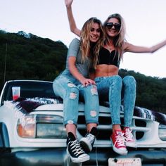 two women sitting on the hood of a pickup truck with their arms in the air