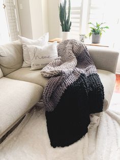 a white couch covered in blankets and pillows next to a potted houseplant