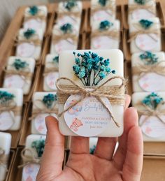 a hand holding a small square soap bar with blue flowers on it in front of rows of baby's breath candles