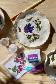 various crafting supplies are laid out on a wooden table, including paper plates and paintbrushes