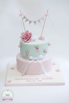 a three tiered cake with pink flowers and bunting on top, sitting on a white surface