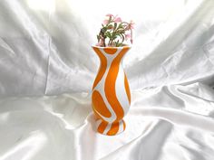 an orange and white vase with flowers in it on a white cloth covered tablecloth