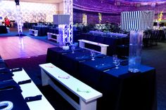 an empty banquet hall with blue tables and white chairs, purple lighting and black tablecloths