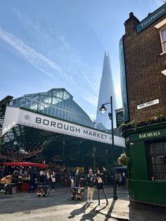 people are walking around in front of the borough market on a sunny day with blue skies