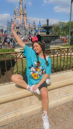 a woman sitting on top of a stone wall in front of a disney mouse castle