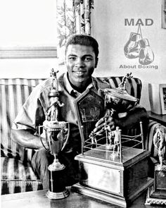 a black and white photo of a man holding trophies in his right hand while sitting on a couch