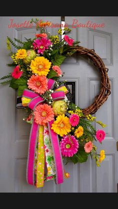 a wreath is hanging on the front door decorated with colorful flowers and greenery,