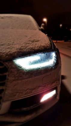 a car that is covered in snow with its headlights turned on and it's headlight glowing